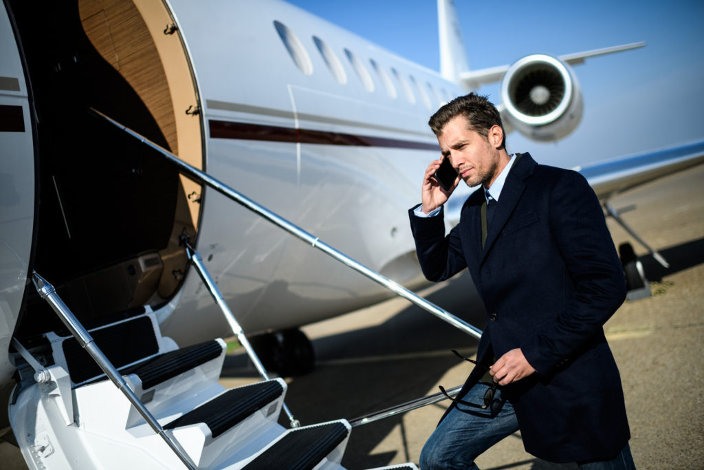 Man wearing elegant clothes standing next to private jet airplane and talking over mobile phone.